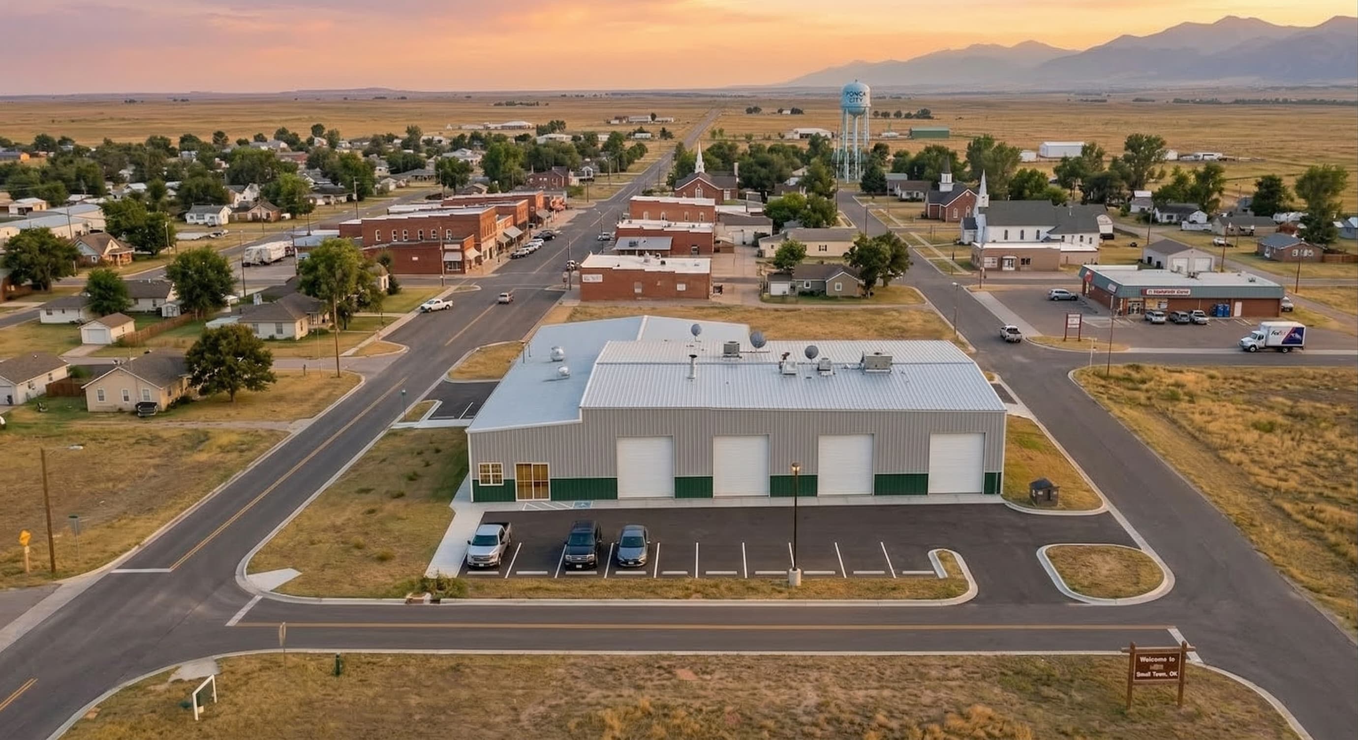 Aerial view of a steel commercial building in a small Oklahoma town at sunset, with green wainscot, multiple overhead doors, and paved parking lot