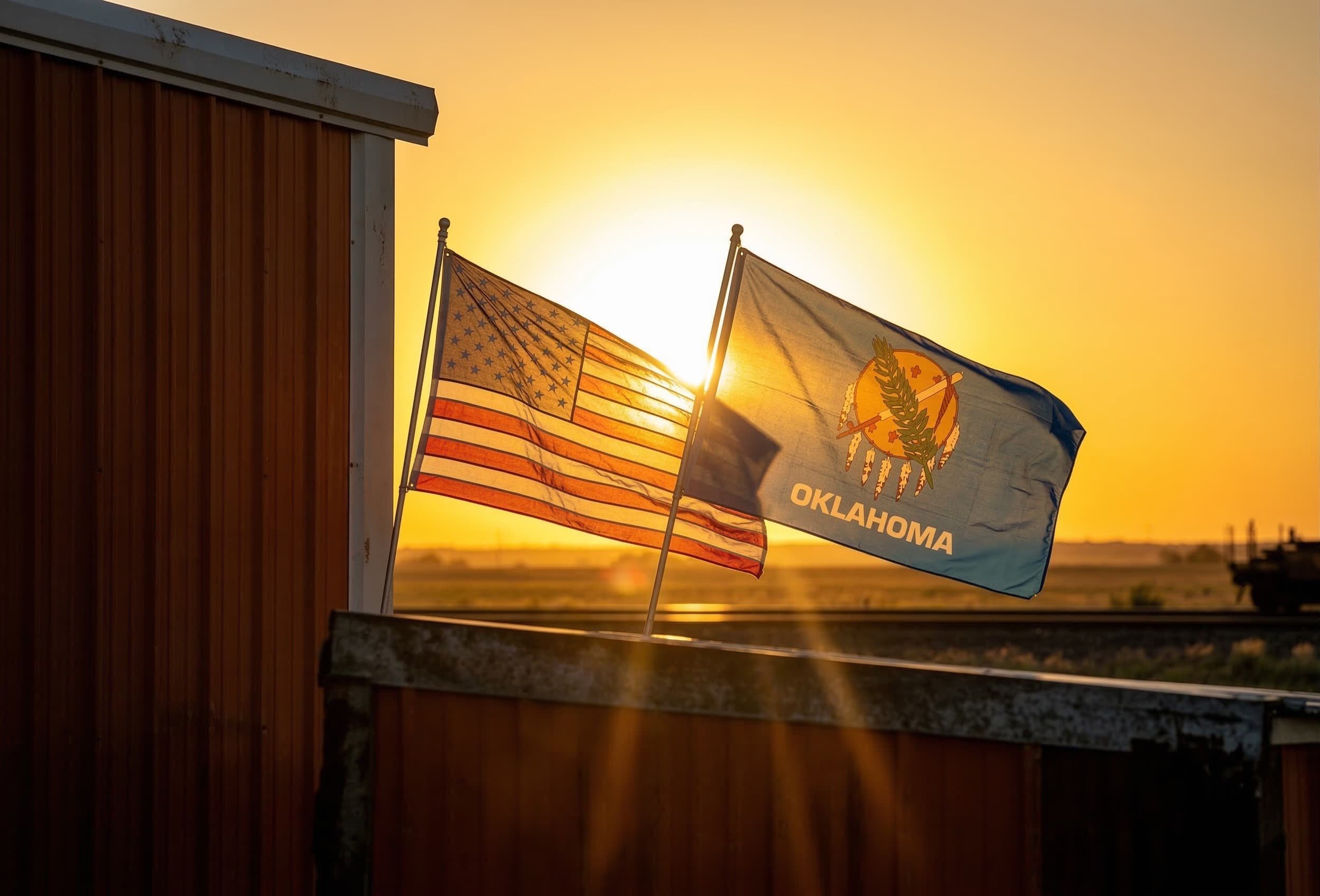American and Oklahoma flags flying at sunset on a steel building in rural Oklahoma